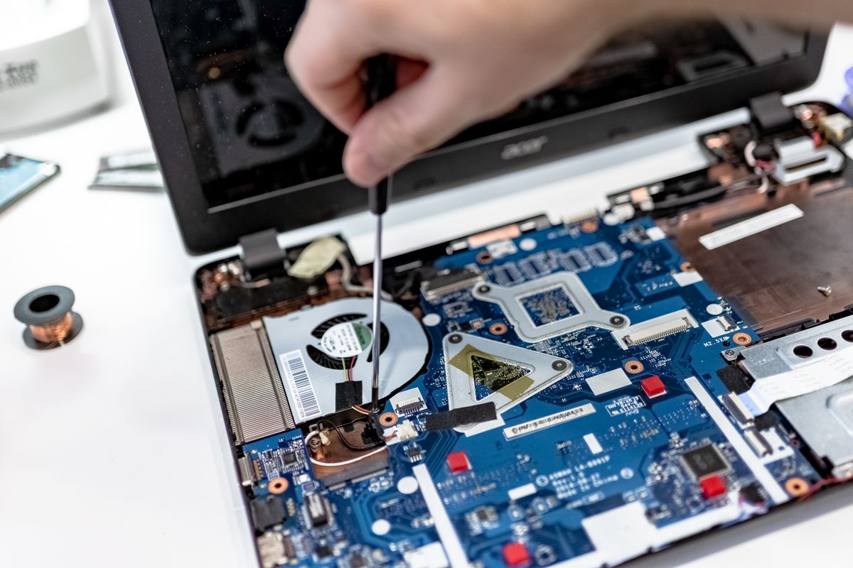 Laptop motherboard being repaired with a screwdriver