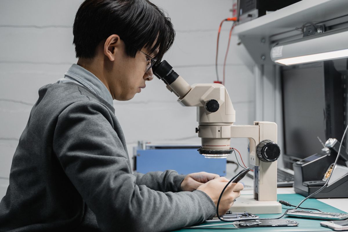 Technician repairing phone motherboard under a microscope